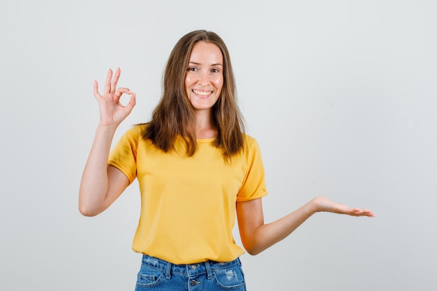 Giovane femmina che mostra gesto giusto con il palmo aperto in maglietta, pantaloncini e allegro