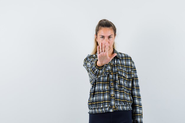 Giovane femmina che mostra il gesto di arresto in camicia, pantaloncini e sembra serio. vista frontale.