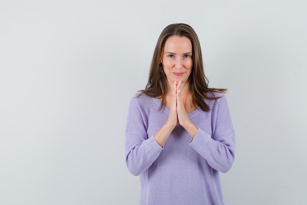 Giovane femmina che mostra il gesto di namaste in camicetta lilla e che sembra soddisfatta