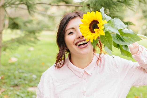 Giovane femmina che sorride e che copre occhio con il girasole