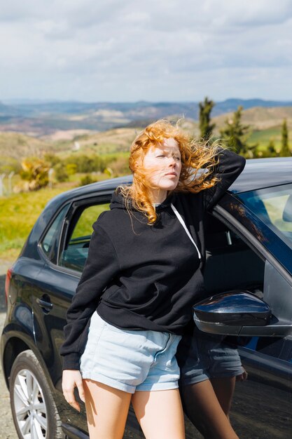 Giovane femmina che sta vicino all&#39;automobile nera