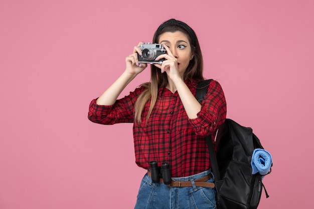 Giovane femmina di vista frontale che cattura maschera con la macchina fotografica sul colore rosa della foto della donna del pavimento