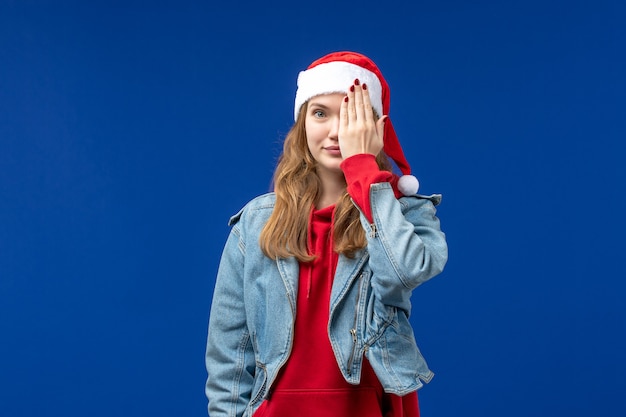 Giovane femmina di vista frontale che copre metà del suo viso su sfondo blu colore di emozione di Natale