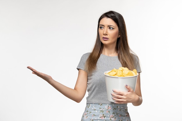 Giovane femmina di vista frontale che mangia cips e che guarda film sulla superficie bianca