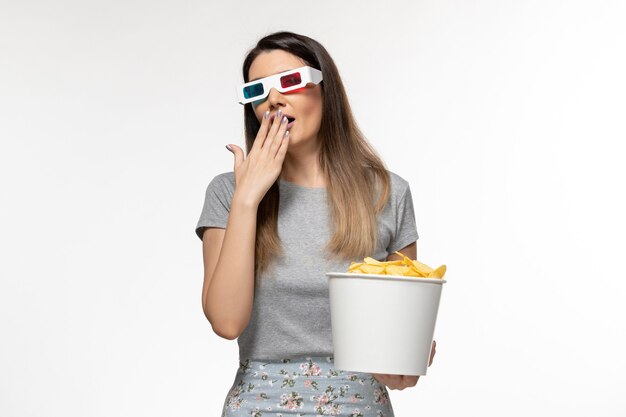 Giovane femmina di vista frontale che mangia cips mentre guarda film in occhiali da sole d su superficie bianca chiara