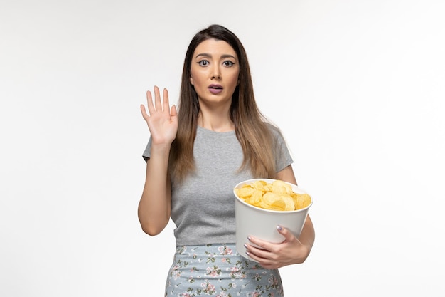 Giovane femmina di vista frontale che mangia patatine fritte che guarda film sulla superficie bianca