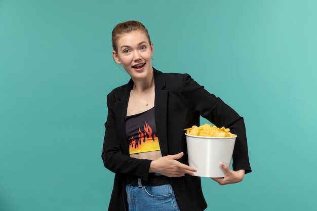 Giovane femmina di vista frontale che mangia patatine fritte che guarda film sulla superficie blu-chiaro