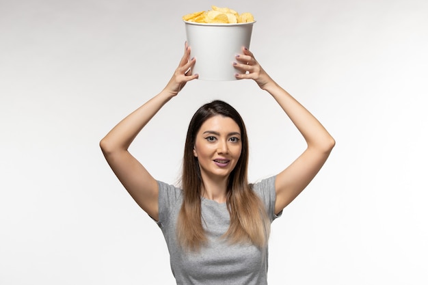 Giovane femmina di vista frontale che mangia patatine fritte che guarda film sullo scrittorio bianco