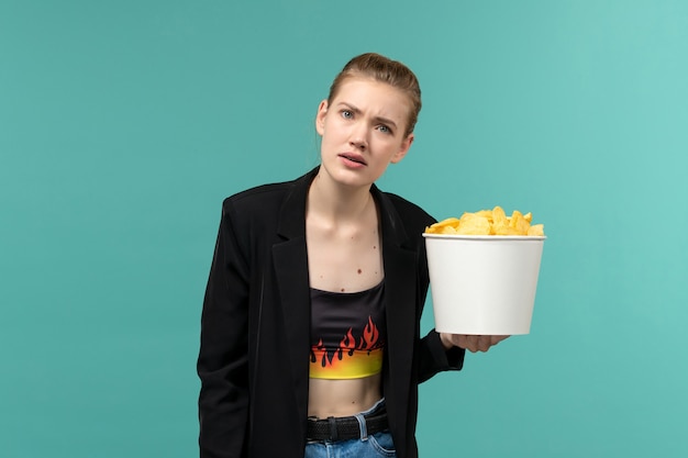 Giovane femmina di vista frontale che mangia patatine fritte che guarda film sullo scrittorio blu