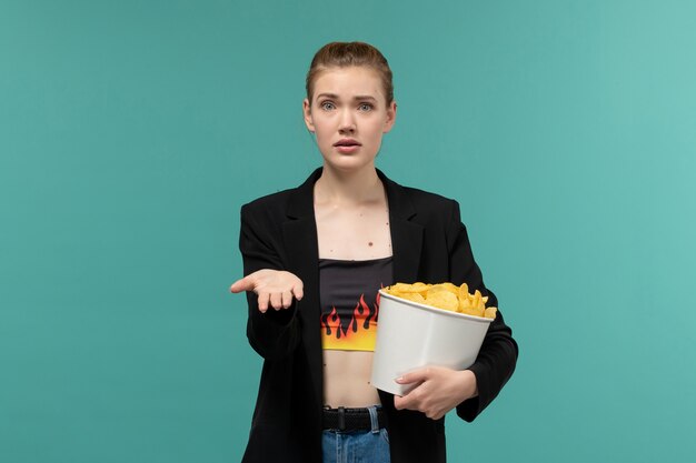 Giovane femmina di vista frontale che mangia patatine fritte che guardano film sulla superficie blu