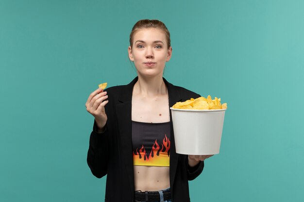 Giovane femmina di vista frontale che mangia patatine fritte che guardano film sulla superficie blu