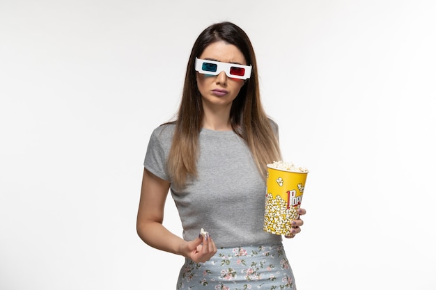 Giovane femmina di vista frontale che mangia popcorn e che guarda film in occhiali da sole d sullo scrittorio bianco
