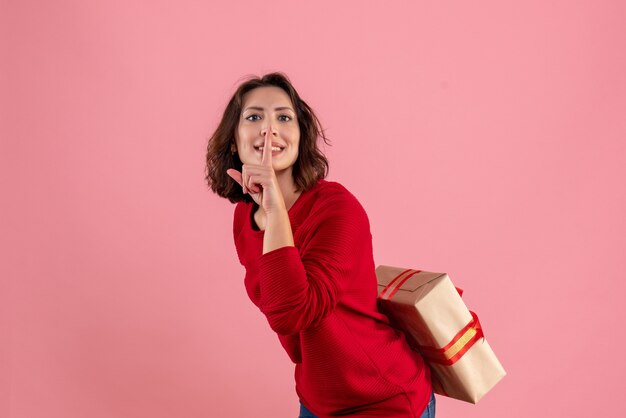 Giovane femmina di vista frontale che nasconde il natale presente dietro la schiena sul rosa