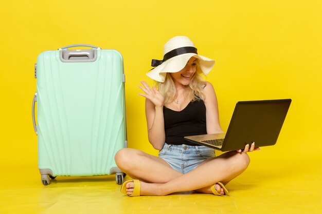 Giovane femmina di vista frontale che per mezzo del suo computer portatile sul sole di viaggio femminile di viaggio di viaggio di vacanza di viaggio della parete gialla