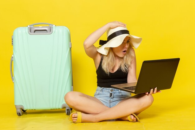 Giovane femmina di vista frontale che per mezzo del suo computer portatile sul sole di viaggio femminile di viaggio di viaggio di vacanza di viaggio della parete gialla