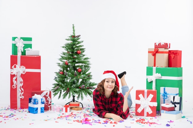 Giovane femmina di vista frontale che pone intorno ai regali di Natale e al piccolo albero di festa sulla neve bianca di natale del nuovo anno di colore della donna del fondo