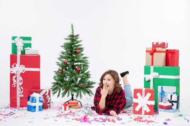 Giovane femmina di vista frontale che pone intorno ai regali di Natale e all'albero di festa su fondo bianco Natale capodanno regalo colore neve emozione