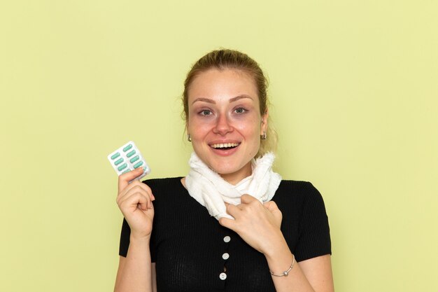 Giovane femmina di vista frontale che si sente molto malato e malato che tiene le pillole e che sorride sulla malattia della medicina femminile della malattia della parete verde