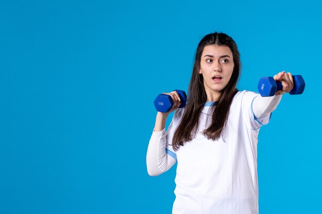 Giovane femmina di vista frontale che tiene i dumbbells blu