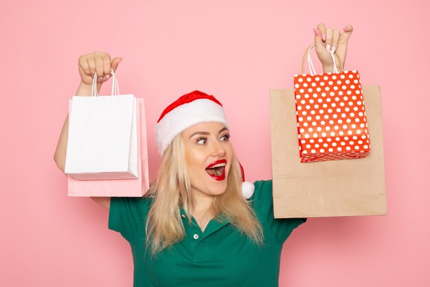 Giovane femmina di vista frontale che tiene i regali di Natale in pacchetti sul nuovo anno rosa del modello della foto di natale della parete