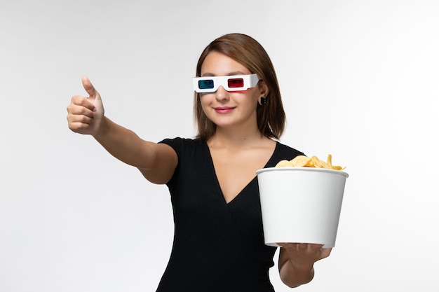 Giovane femmina di vista frontale che tiene le patatine fritte in occhiali da sole di d e guardare film che sorride sulla superficie bianca
