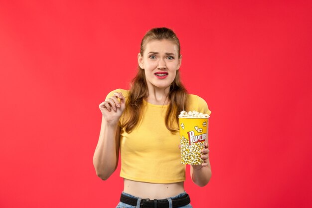 Giovane femmina di vista frontale che tiene popcorn sul film rosso chiaro del cinema del cinema della parete