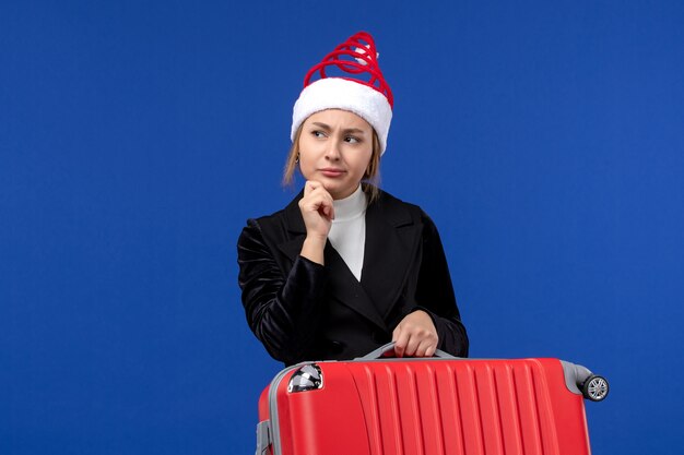 Giovane femmina di vista frontale che trasporta borsa rossa sulla donna blu di viaggio di vacanza di vacanza dello scrittorio