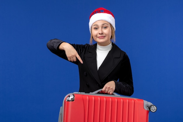 Giovane femmina di vista frontale che trasporta borsa rossa sulla donna di vacanza di vacanza di viaggio della parete blu