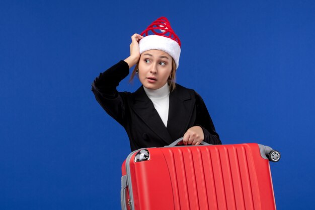 Giovane femmina di vista frontale che trasporta borsa rossa sulla donna di viaggio di vacanza di vacanza della parete blu