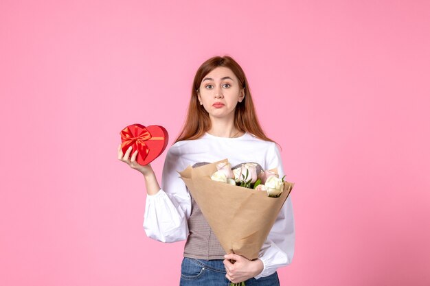 Giovane femmina di vista frontale con i fiori e presente come regalo di giorno delle donne su fondo rosa amore della donna data femminile sensuale di uguaglianza orizzontale di marzo