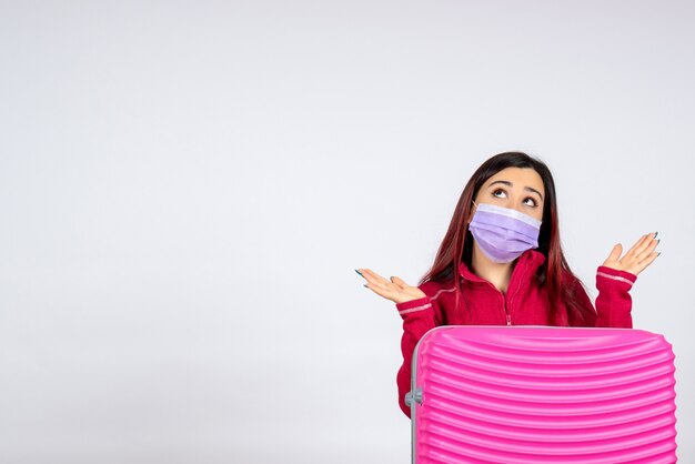 Giovane femmina di vista frontale con il sacchetto rosa nella maschera sterile sul virus della donna covid di vacanza di colore di viaggio della parete bianca