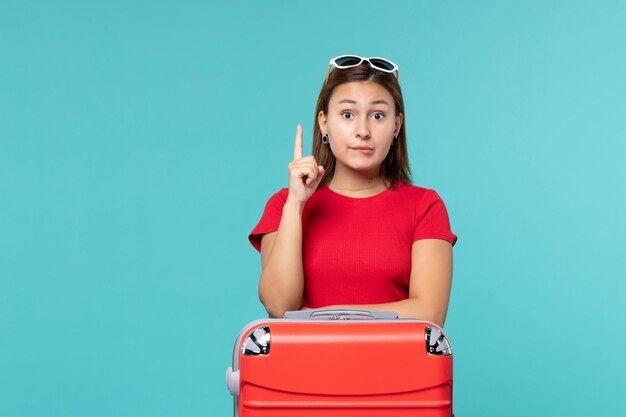 Giovane femmina di vista frontale con il sacchetto rosso che prepara per la vacanza sullo spazio blu-chiaro