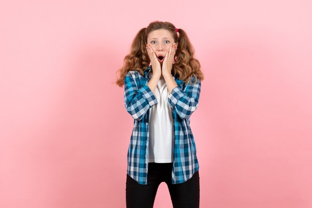 Giovane femmina di vista frontale in camicia a scacchi blu che posa sul colore rosa della donna del modello di emozione della gioventù del bambino dello scrittorio