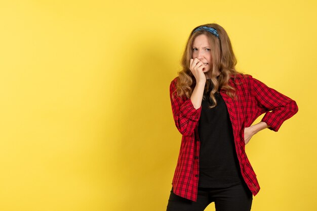 Giovane femmina di vista frontale in camicia a scacchi rossa che sta sulla donna di modello di colore umano delle ragazze dello scrittorio giallo