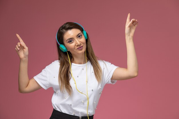 Giovane femmina di vista frontale in camicia bianca che ascolta la musica e che posa sulla parete rosa, modello di posa della donna di colore