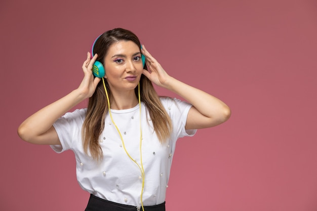 Giovane femmina di vista frontale in camicia bianca che ascolta la musica sulla parete rosa, donna di modello di posa della donna di colore