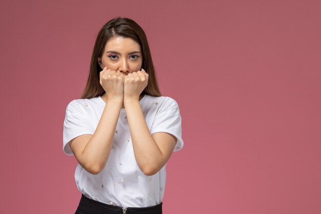 Giovane femmina di vista frontale in camicia bianca che posa con i pugni stretti sul muro rosa, posa della donna del modello di colore