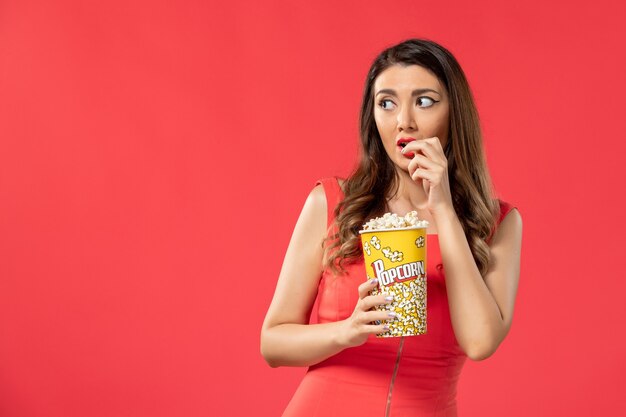 Giovane femmina di vista frontale in camicia rossa che mangia popcorn guardando film sulla superficie rossa