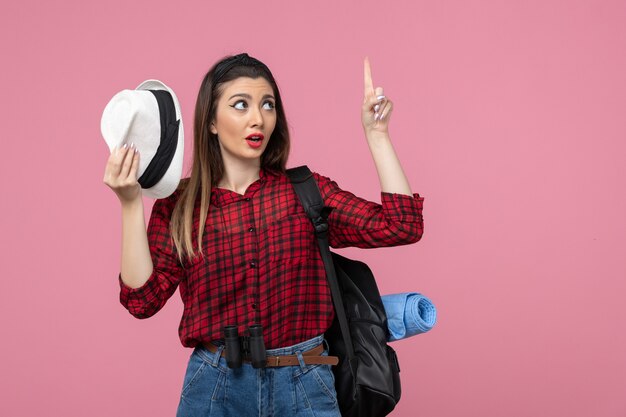 Giovane femmina di vista frontale in camicia rossa con il cappello sul colore della donna umana di sfondo rosa