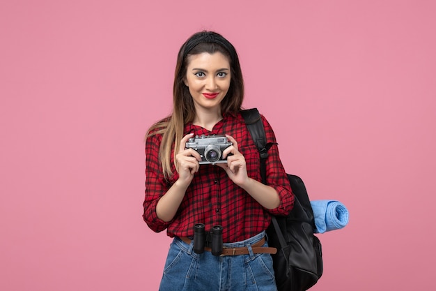 Giovane femmina di vista frontale in camicia rossa con la macchina fotografica sulla donna rosa della foto del modello dello scrittorio