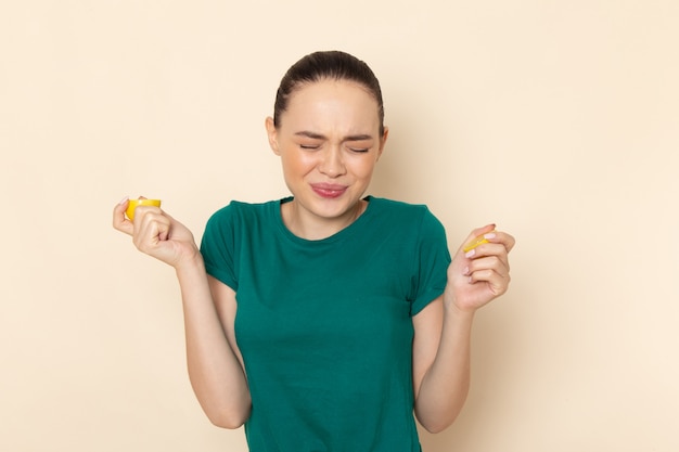 Giovane femmina di vista frontale in camicia verde scuro e blue jeans che morde il limone sul beige