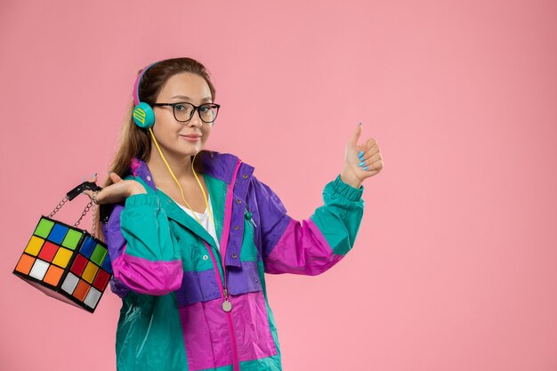 Giovane femmina di vista frontale in cappotto colorato della maglietta bianca che ascolta la musica tramite le cuffie che sorridono su fondo rosa