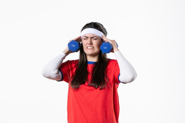 Giovane femmina di vista frontale in vestiti di sport che risolve con i dumbbells sulla parete bianca