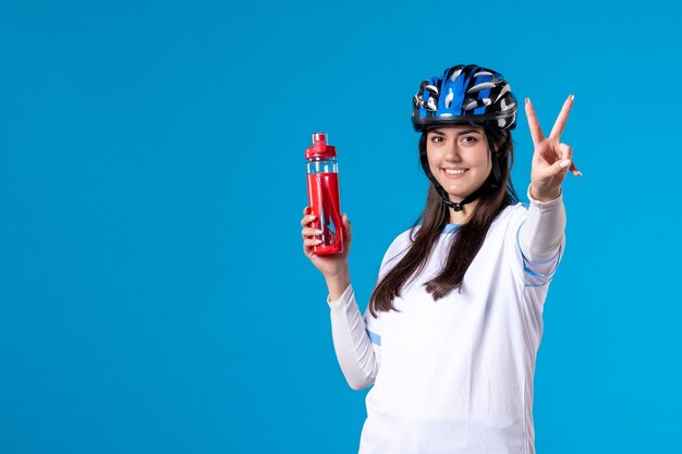 Giovane femmina di vista frontale in vestiti di sport con il casco sulla parete blu