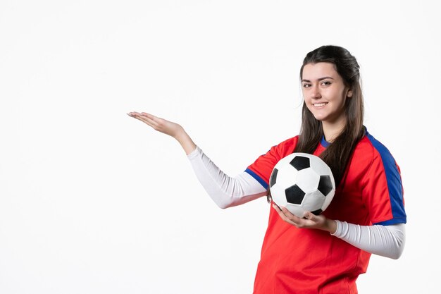 Giovane femmina di vista frontale in vestiti di sport con il pallone da calcio sulla parete bianca