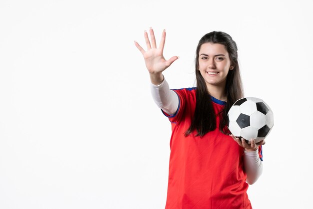 Giovane femmina di vista frontale in vestiti di sport con il pallone da calcio sulla parete bianca