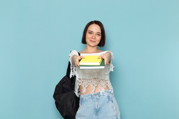 giovane femmina in camicia bianca blue jeans e borsa nera in possesso di quaderni in posa sorridente sul blu