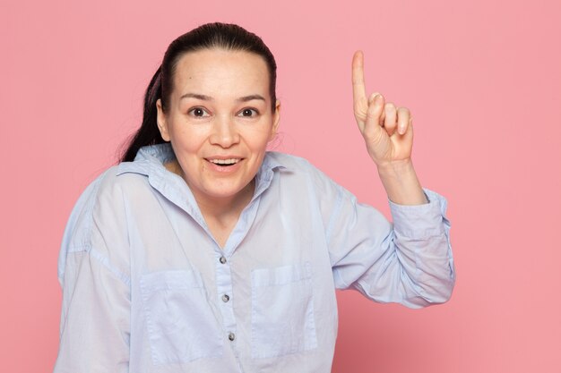 giovane femmina in camicia blu in posa sul muro rosa