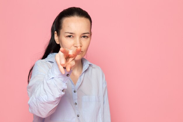 giovane femmina in camicia blu in posa sul muro rosa