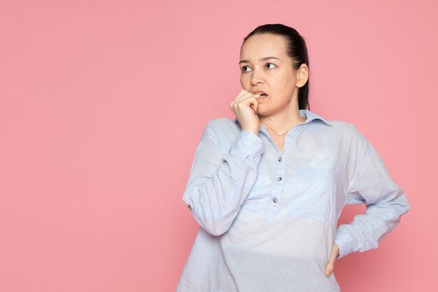 giovane femmina in camicia blu in posa sul muro rosa